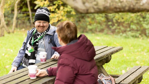 Visitors sat at a table with hot drinks in the garden at Attingham Park, Shropshire with a tree branch in the foreground
